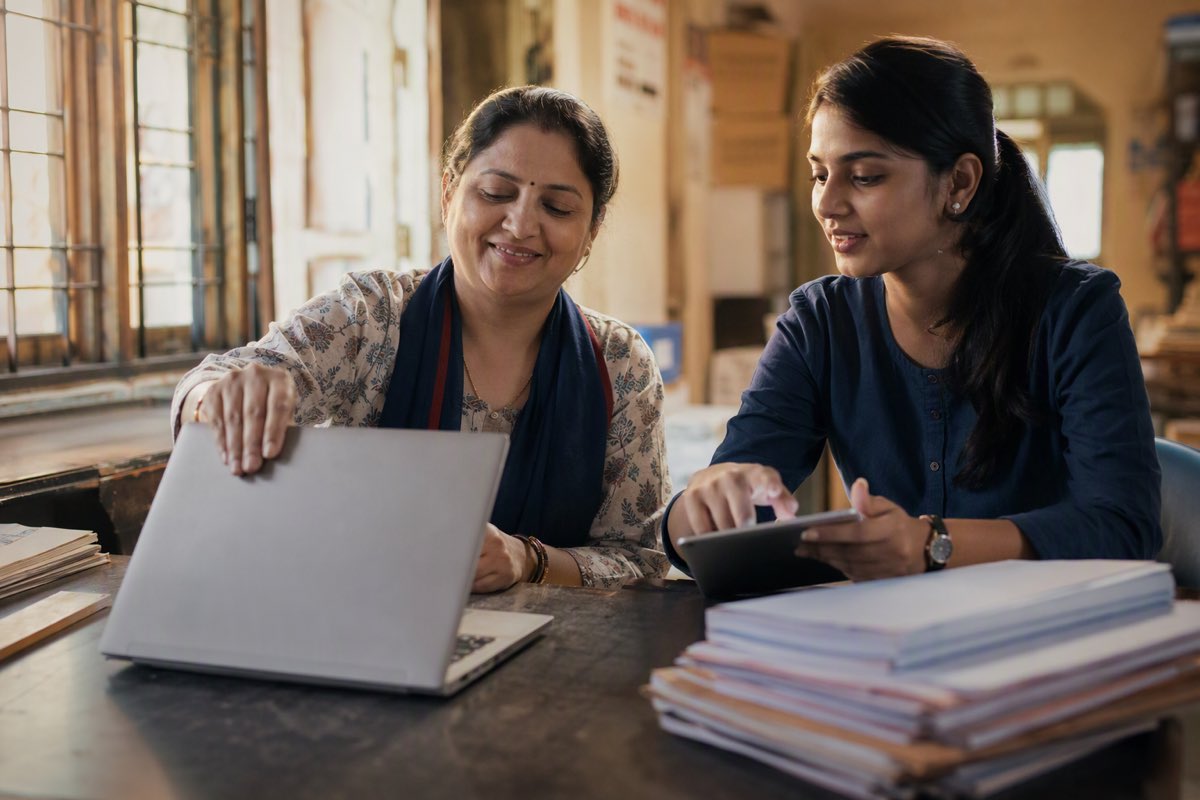 A sales operations manager closing her laptop at month end while a colleague approves the last scheme payouts on a tablet