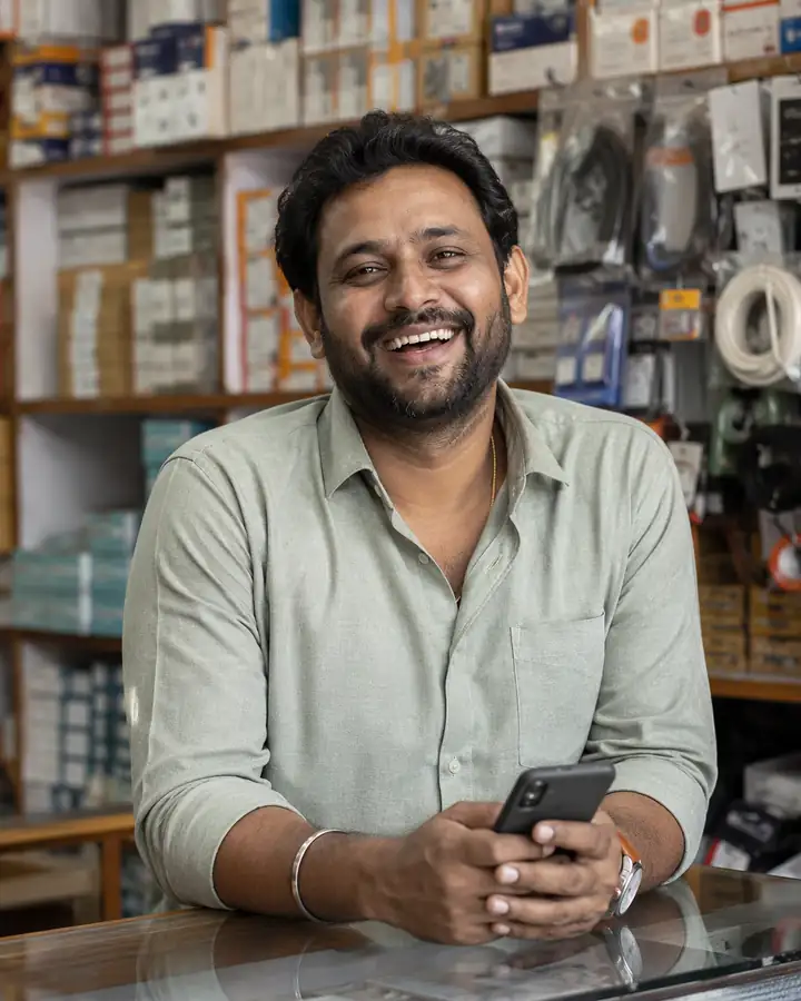 A happy retailer behind the counter of his hardware store holding his phone