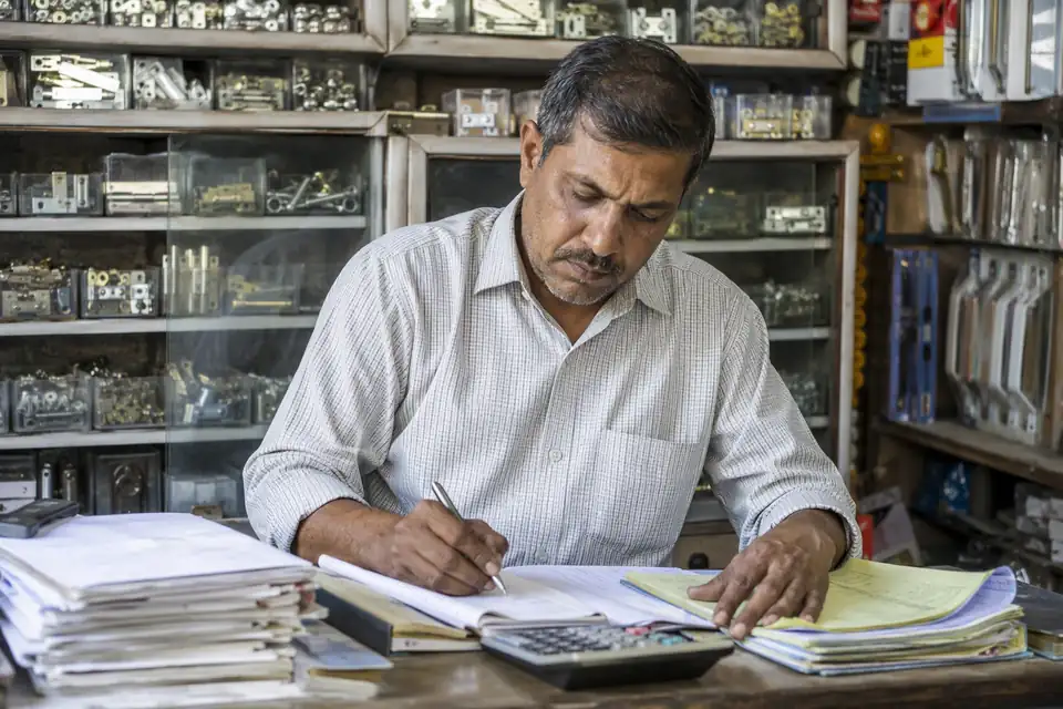 A Furniture Fittings & Hardware channel partner working out incentives by hand with paper circulars and registers